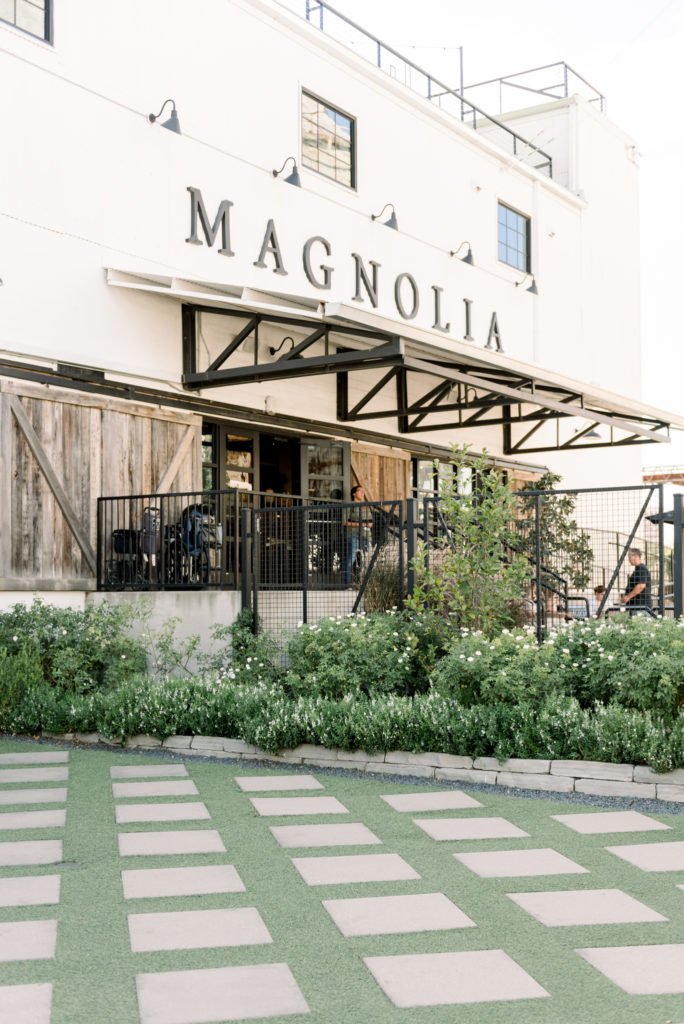 The Magnolia Market at the Silos | The entry of the magnolia market | Concrete pavers with symmetrical lines of exposed grass in between. The building is white with black accents, black metal beams for the roof & fencing.
